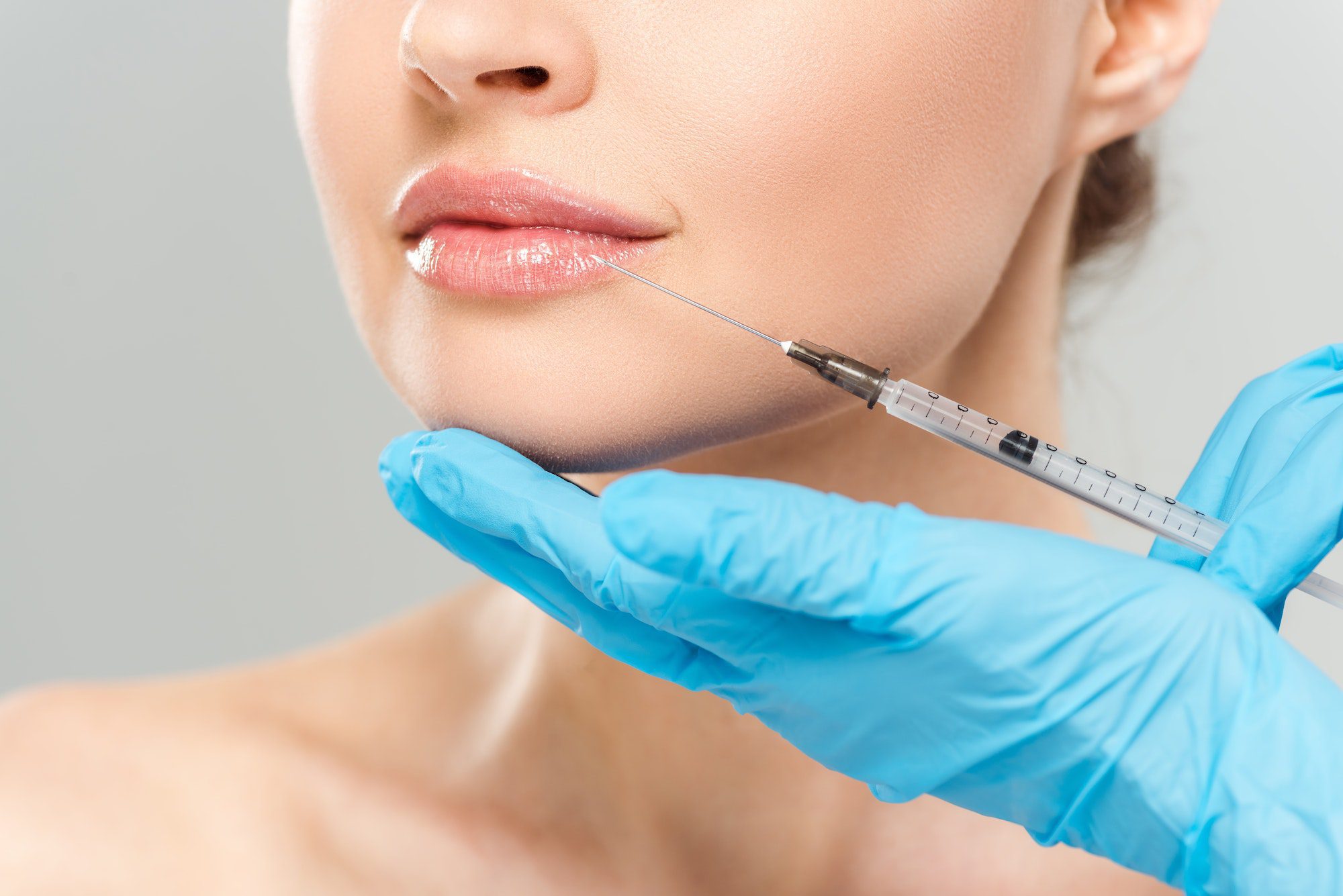 cropped view of cosmetologist in blue latex gloves holding syringe near face of woman isolated on